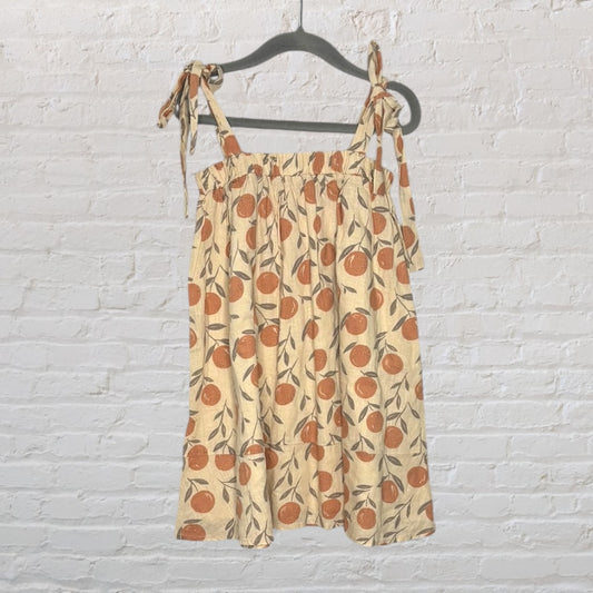 Sleeveless beige dress with orange floral print and tie straps, hanging on a dark hanger.