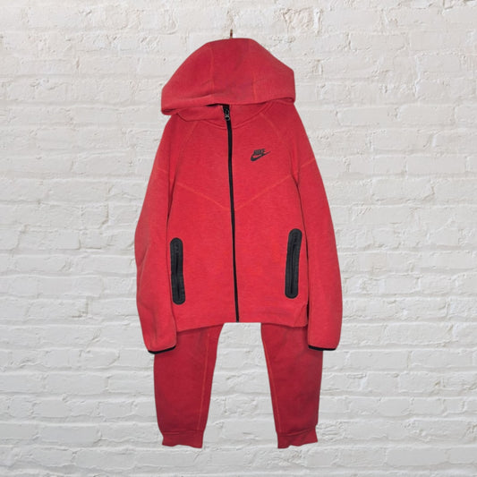 Red Nike full-zip hoodie and sweatpants set with black accents, displayed on a white brick wall.