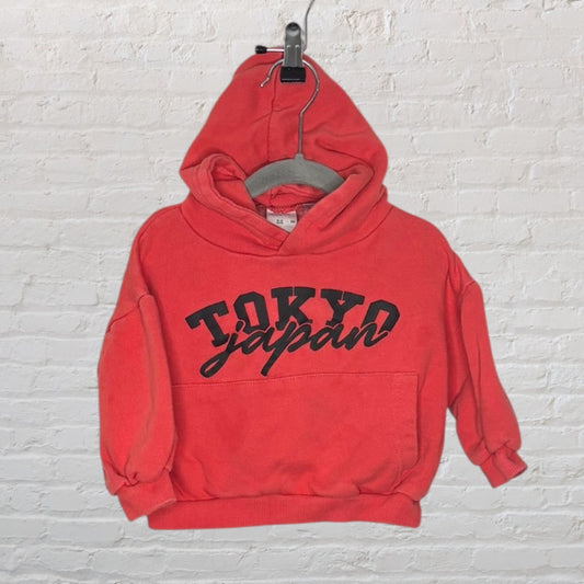 Red hoodie with 'Tokyo Japan' graphic text on the front, displayed against a white brick background.