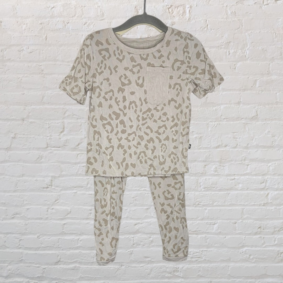 A beige and light brown leopard print pajama set featuring a short-sleeve top with a pocket and matching pants, hanging on a dark hanger.