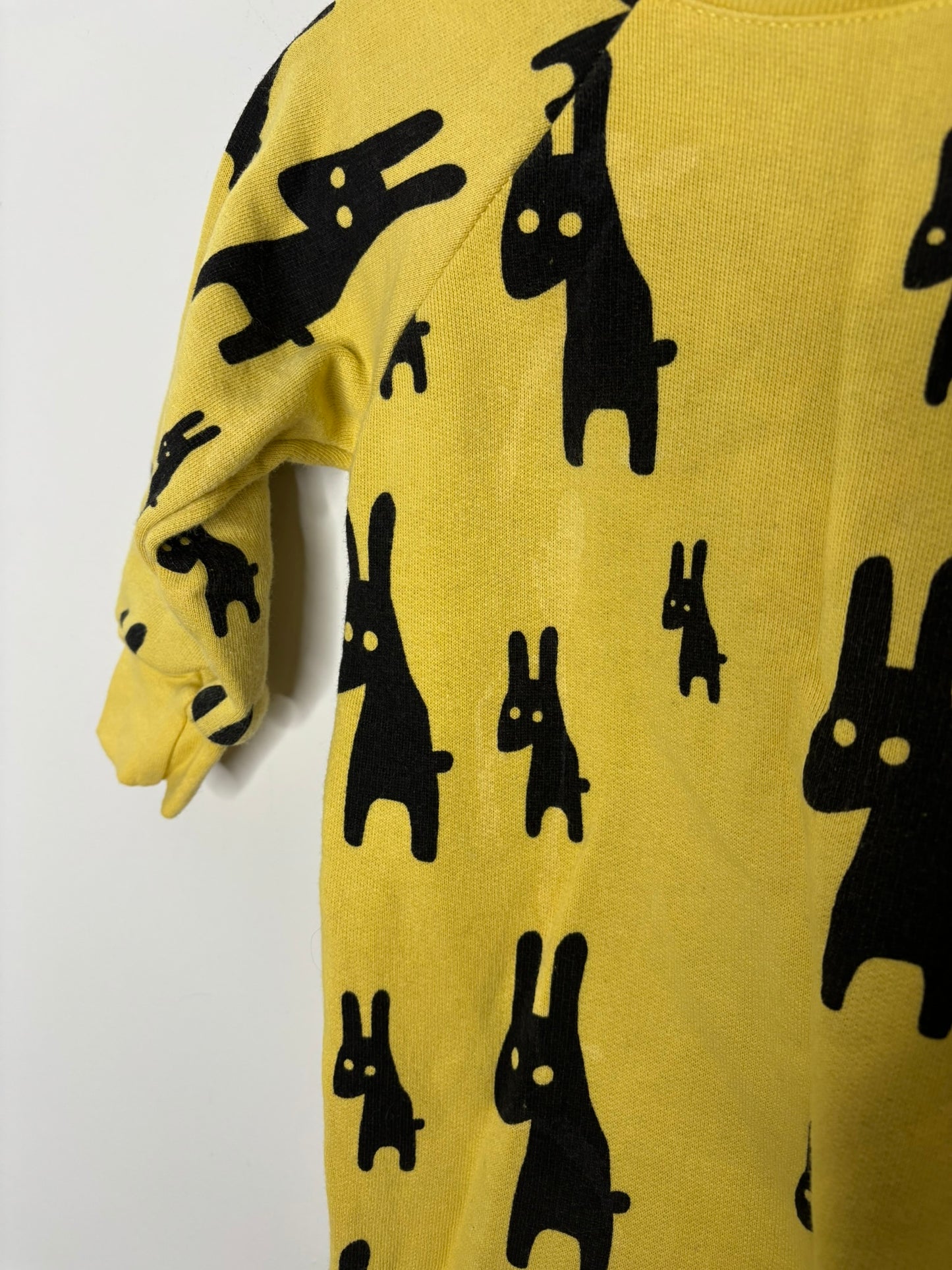 Yellow onepiece suit with black rabbit pattern for infants, displayed on a hanger against a white brick wall.