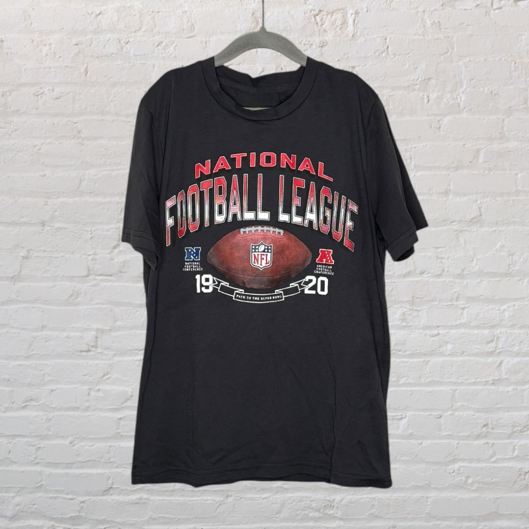 Black NFL T-shirt with National Football League text and football graphic, hung against a brick wall.