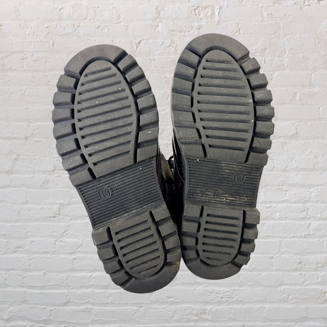 Pair of iridescent combat boots with black laces and thick soles against a white brick wall.