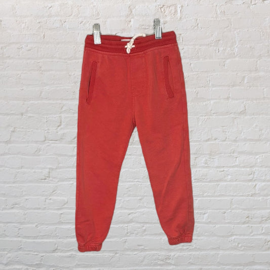 Red drawstring sweatpants with elastic cuffs and pockets, hanging against a brick wall.