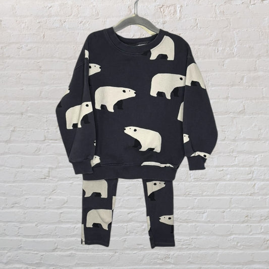 Unisex black outfit with polar bear prints, including a top and matching bottoms, hanging on a hanger against a white brick wall.
