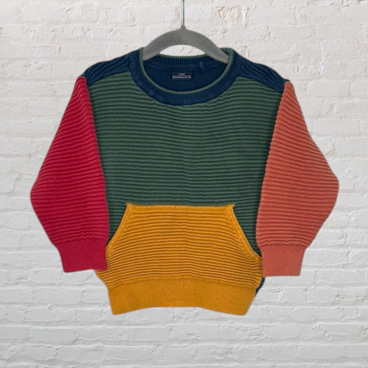 Unisex colorblock sweater with ribbed knit texture, featuring green, red, orange, and yellow panels, displayed on a gray hanger.