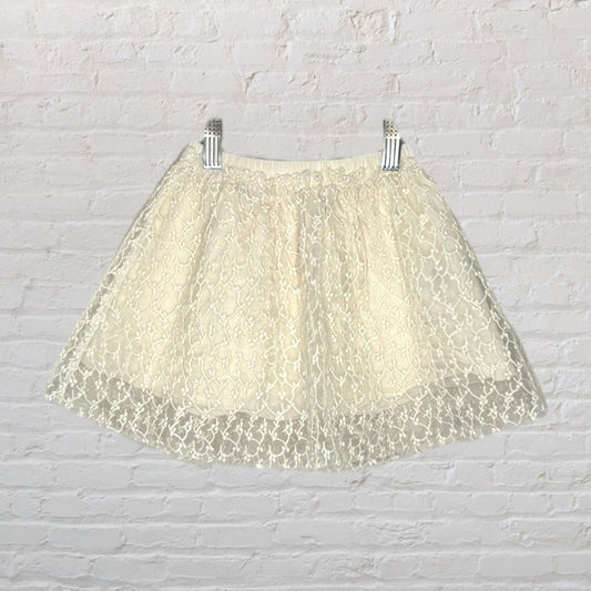 Cream skirt with lace overlay design hanging against a brick wall.