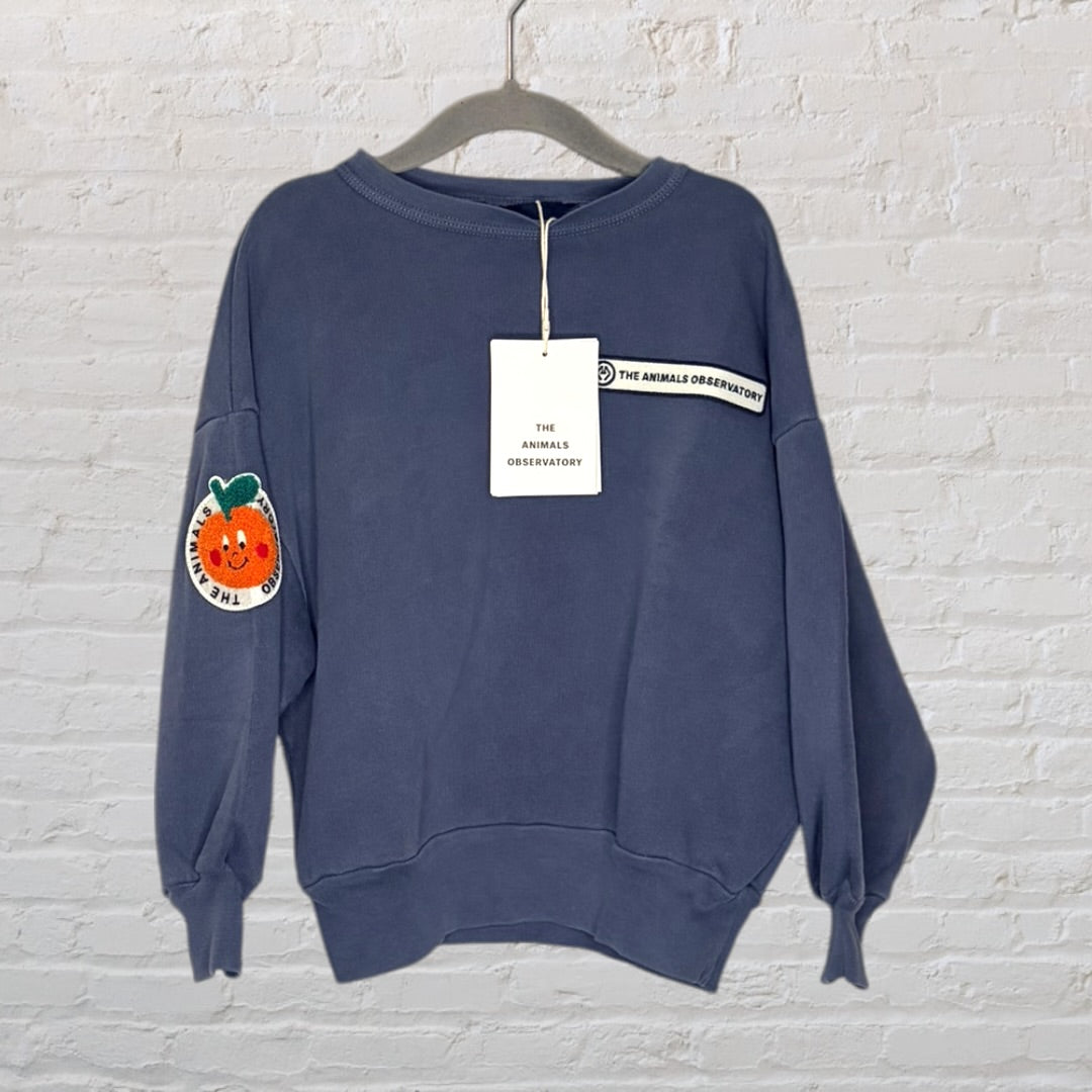 Navy sweatshirt by The Animals Observatory with a cheerful orange patch on the sleeve, displayed on a hanger with tags attached.