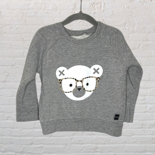 Grey sweatshirt with a cute bear graphic wearing glasses, hanging against a brick wall background.