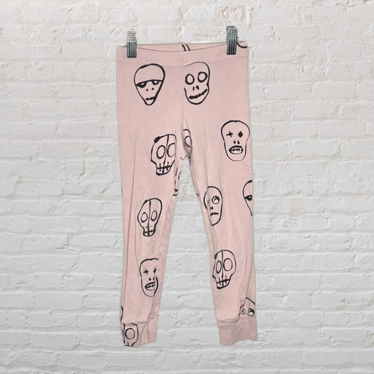 Pink leggings with black skull print design on a white brick wall background.