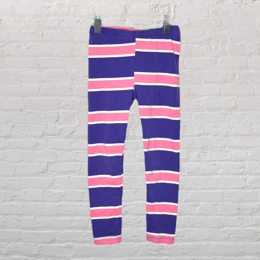 Purple leggings with horizontal pink and white stripes, displayed on a hanger against a white brick wall.