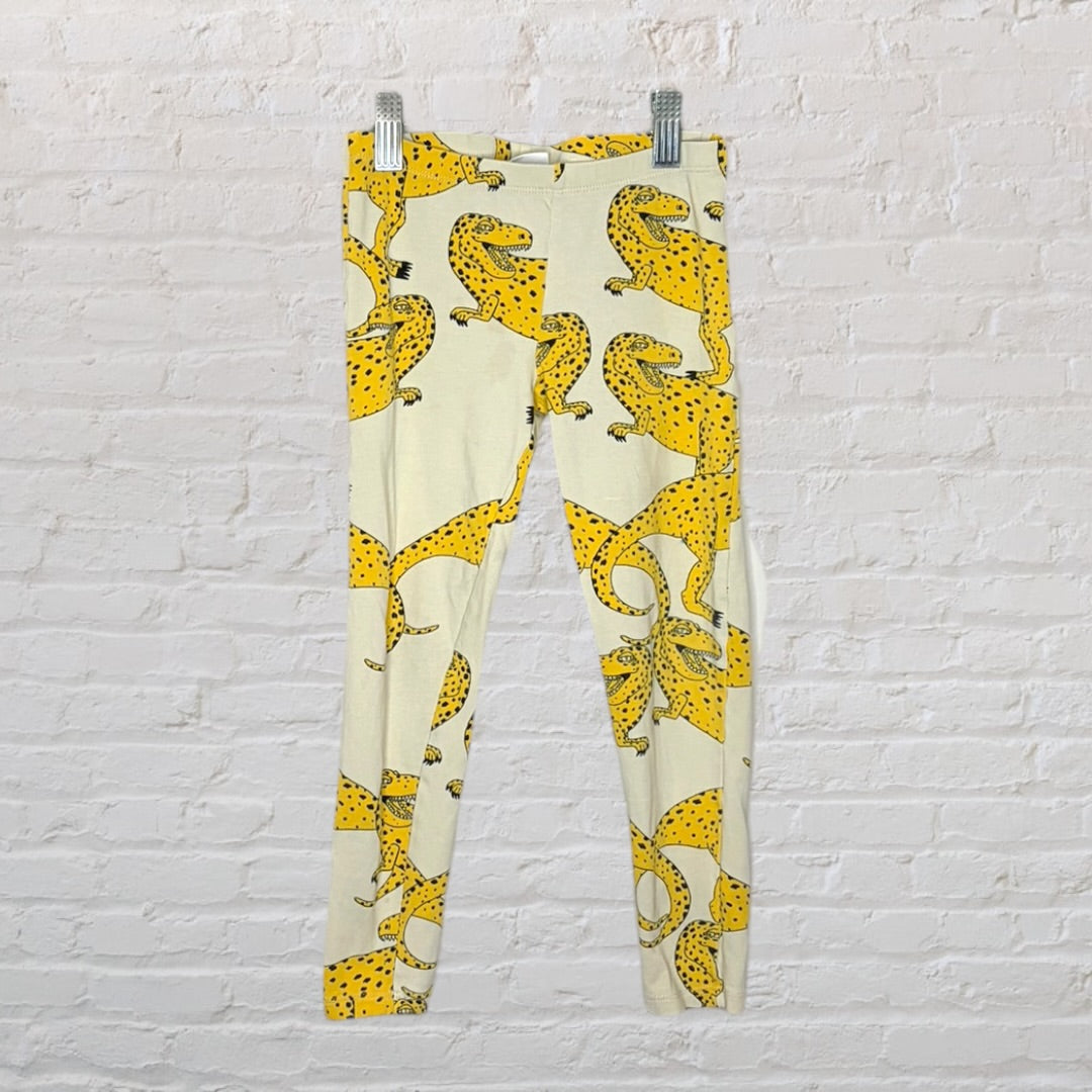 Cream leggings with a bold yellow leopard print, displayed against a white brick wall.