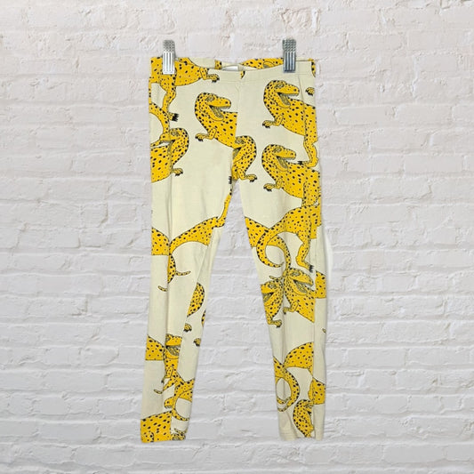 Cream leggings with a bold yellow leopard print, displayed against a white brick wall.