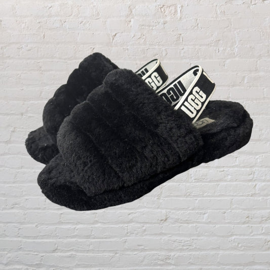 Black fluffy slingback slippers by UGG with elastic UGG-branded strap.