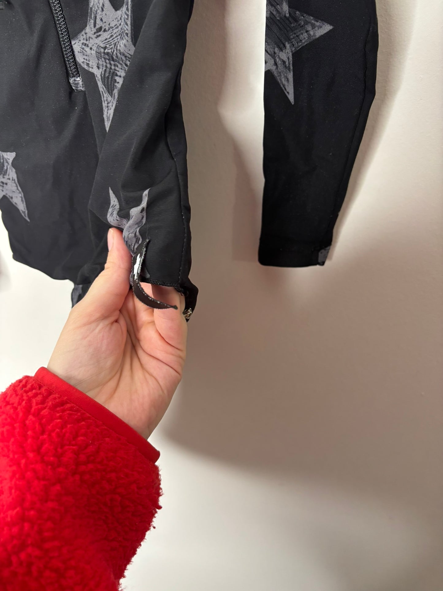 Black long sleeve bodysuit with grey star pattern and front zipper, displayed on a hanger against a brick wall.
