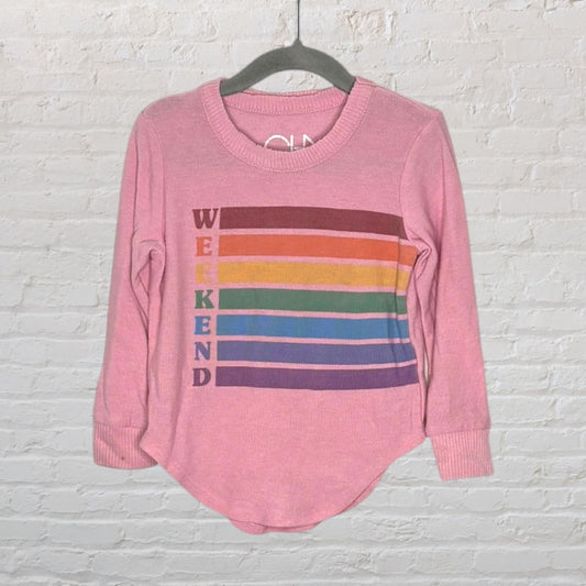 Pink long sleeve shirt with 'Weekend' print and colorful stripes, hanging on a hanger against a brick wall.