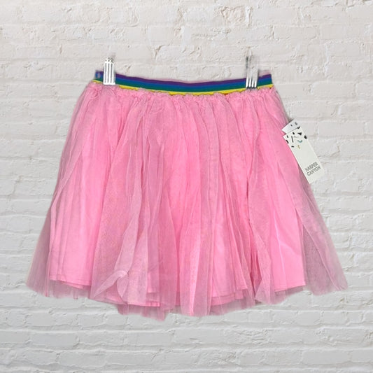 Pink tulle skirt with a rainbow waistband, hanging against a white brick background.