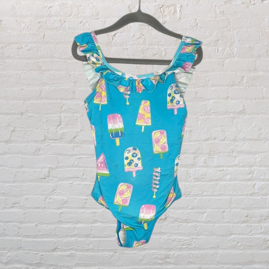 Blue swimsuit with colorful ice cream print and ruffle detailing on the shoulders, hanging on a black hanger.
