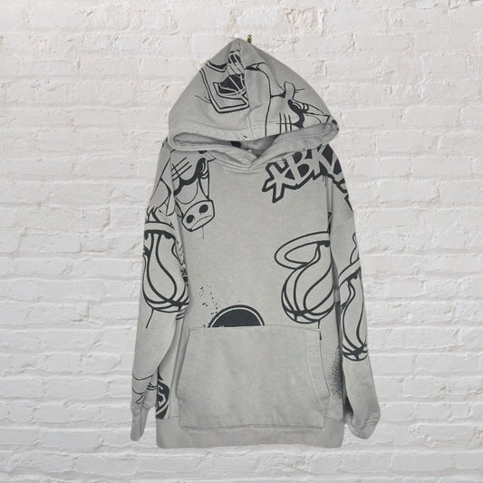 Grey hoodie with black cartoon graphics, featuring a kangaroo pocket and hood, displayed against a brick wall.