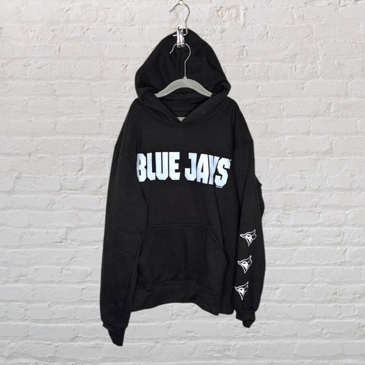 Black Blue Jays hoodie with front print and logo on the sleeve, hung against a brick wall.