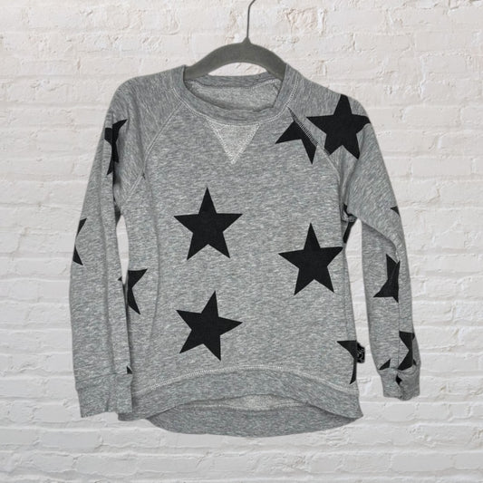 Grey sweatshirt with black star patterns, displayed on a hanger against a white brick wall.