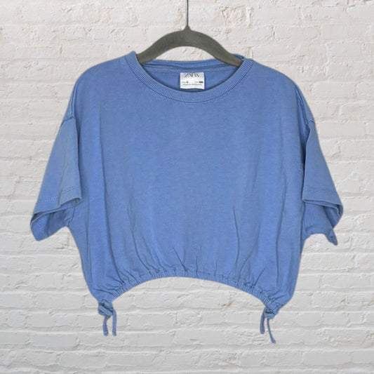 Light blue cropped T-shirt with drawstring hem, short sleeves, and crew neckline displayed on a black hanger.