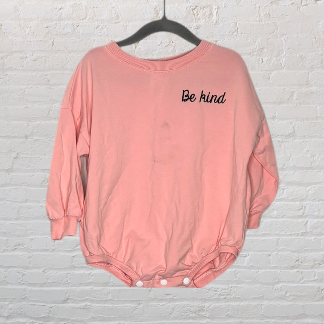 Pink baby onesie with 'Be kind' embroidered on the chest, featuring snap closures at the bottom.