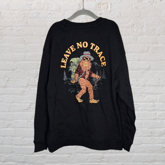Black sweatshirt with 'Leave No Trace' text and a whimsical graphic of a creature with a backpack, displayed on a hanger.