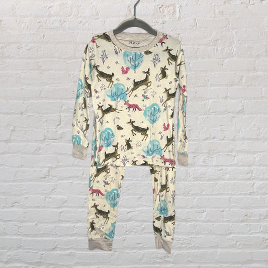 Children's two-piece cream pajama set with forest animal print by Hatley, hanging on a wall.