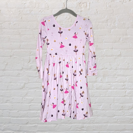 Light pink long sleeve dress with ballerina print pattern, displayed on a hanger against a white brick wall.