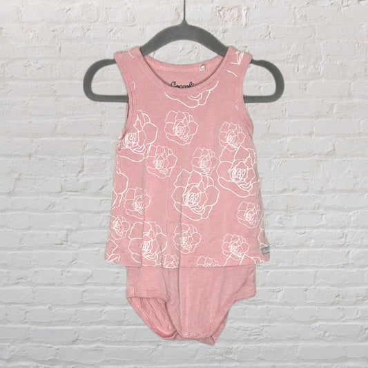 Pink sleeveless infant bodysuit with white floral patterns, displayed on a hanger against a brick background.