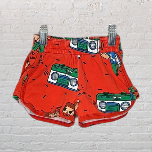Bright orange shorts featuring a playful print of green boomboxes and cartoon characters.