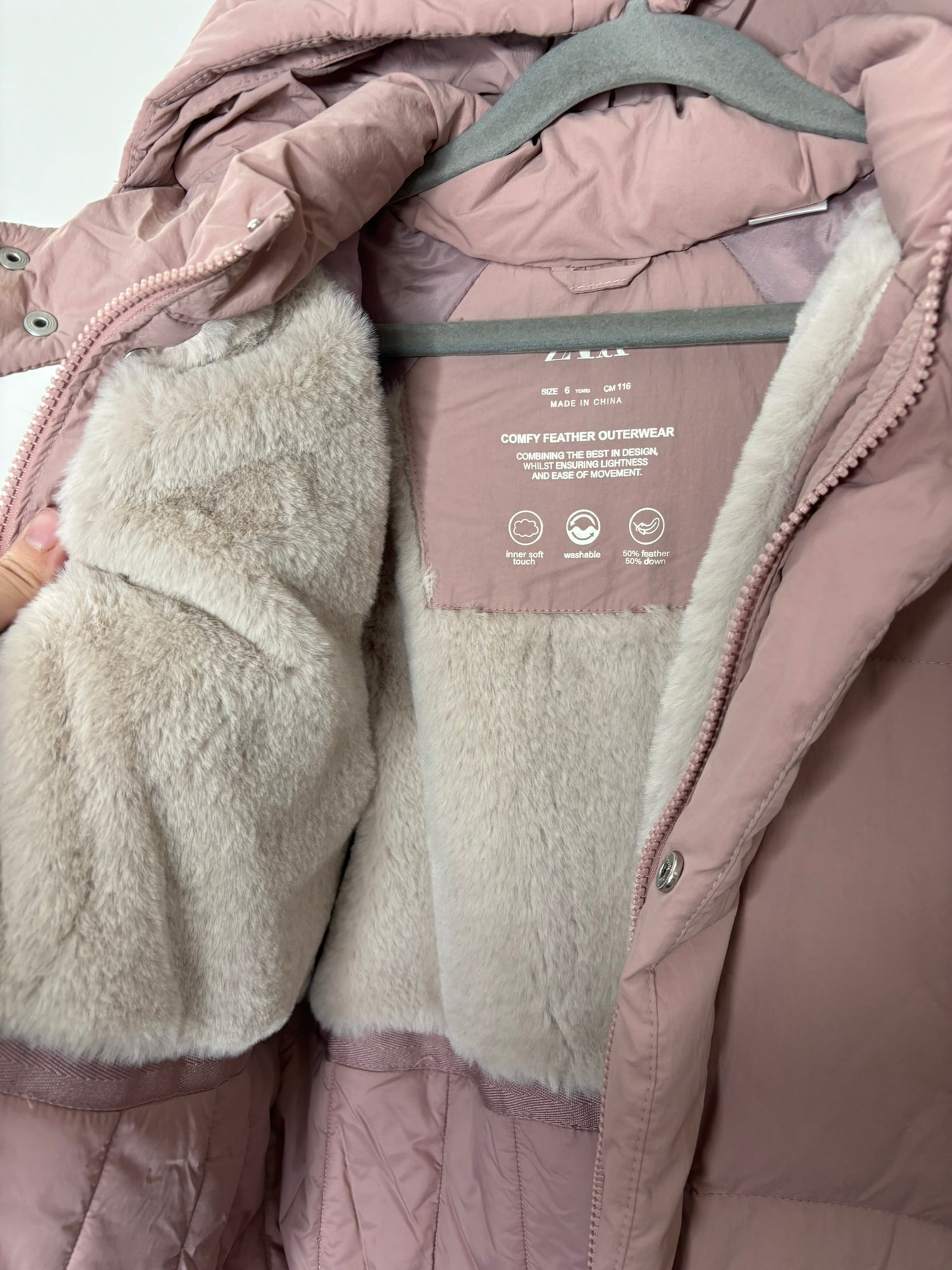 Pink hooded puffer jacket with front snap buttons, displayed on a hanger against a brick wall.