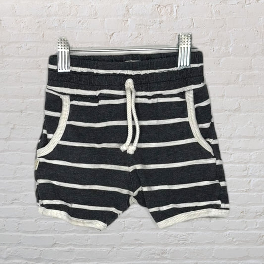 Black and white striped drawstring shorts with pockets, hanging on a clip hanger against a brick wall background.