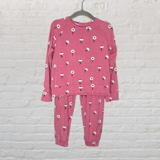 Pink pajama set with white floral design on a hanger against a white brick wall.