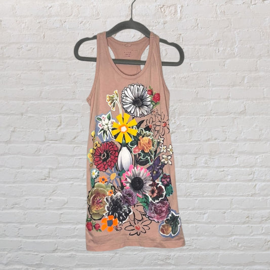 Beige racerback dress with vibrant floral graphics hanging on a hanger against a brick wall.