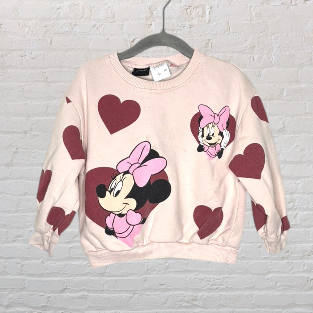 A pink sweatshirt featuring Minnie Mouse graphics and red heart patterns, displayed on a hanger.