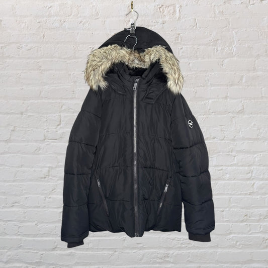 Black puffer jacket with a faux fur hood, hanging against a white brick wall.