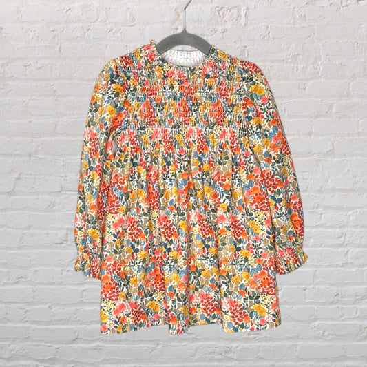 Long-sleeve dress with a vibrant floral pattern and smocked detailing, hanging on a gray hanger.