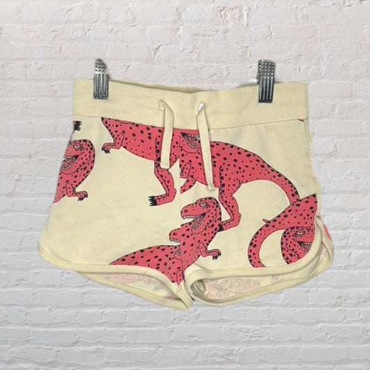 Beige shorts with pink dinosaur print and drawstring waist, hanging on a clip hanger.