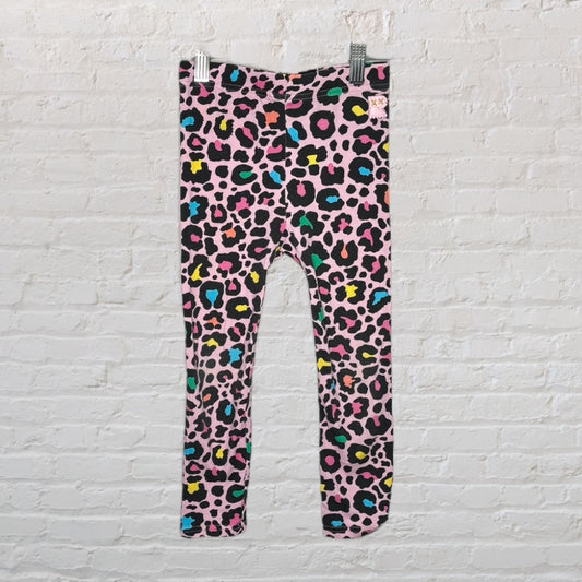 Pink leggings with a vibrant multicolor leopard print pattern hanging on a white brick wall.