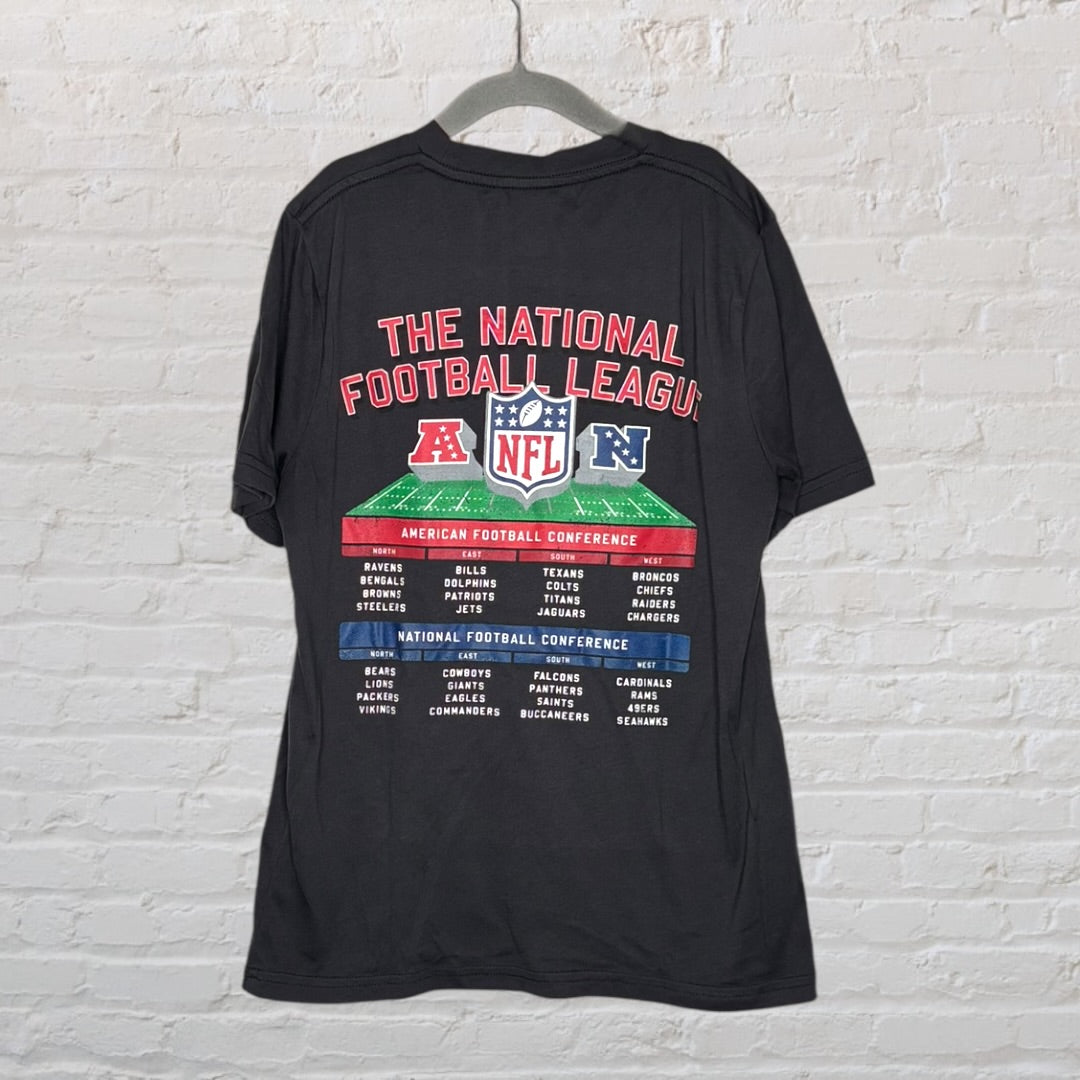Black NFL T-shirt with National Football League text and football graphic, hung against a brick wall.