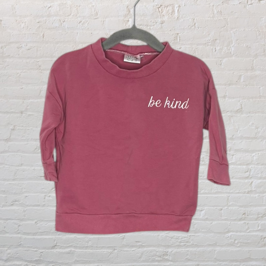 Dusty rose sweatshirt with 'be kind' text on the chest, hung on a hanger.