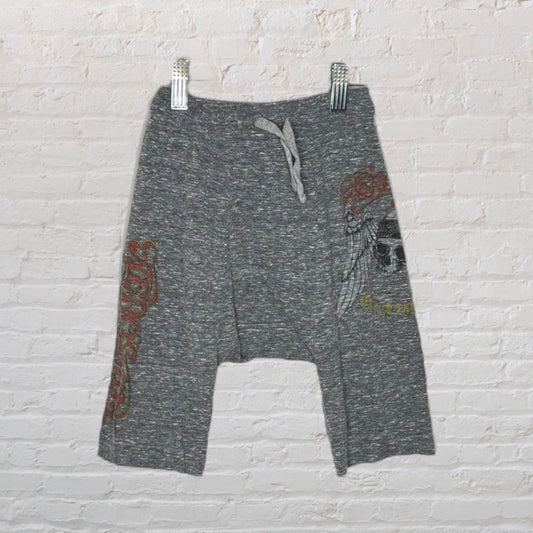 Heather grey drawstring shorts with graphic prints featuring a skull and text, displayed on hangers against a white brick background.