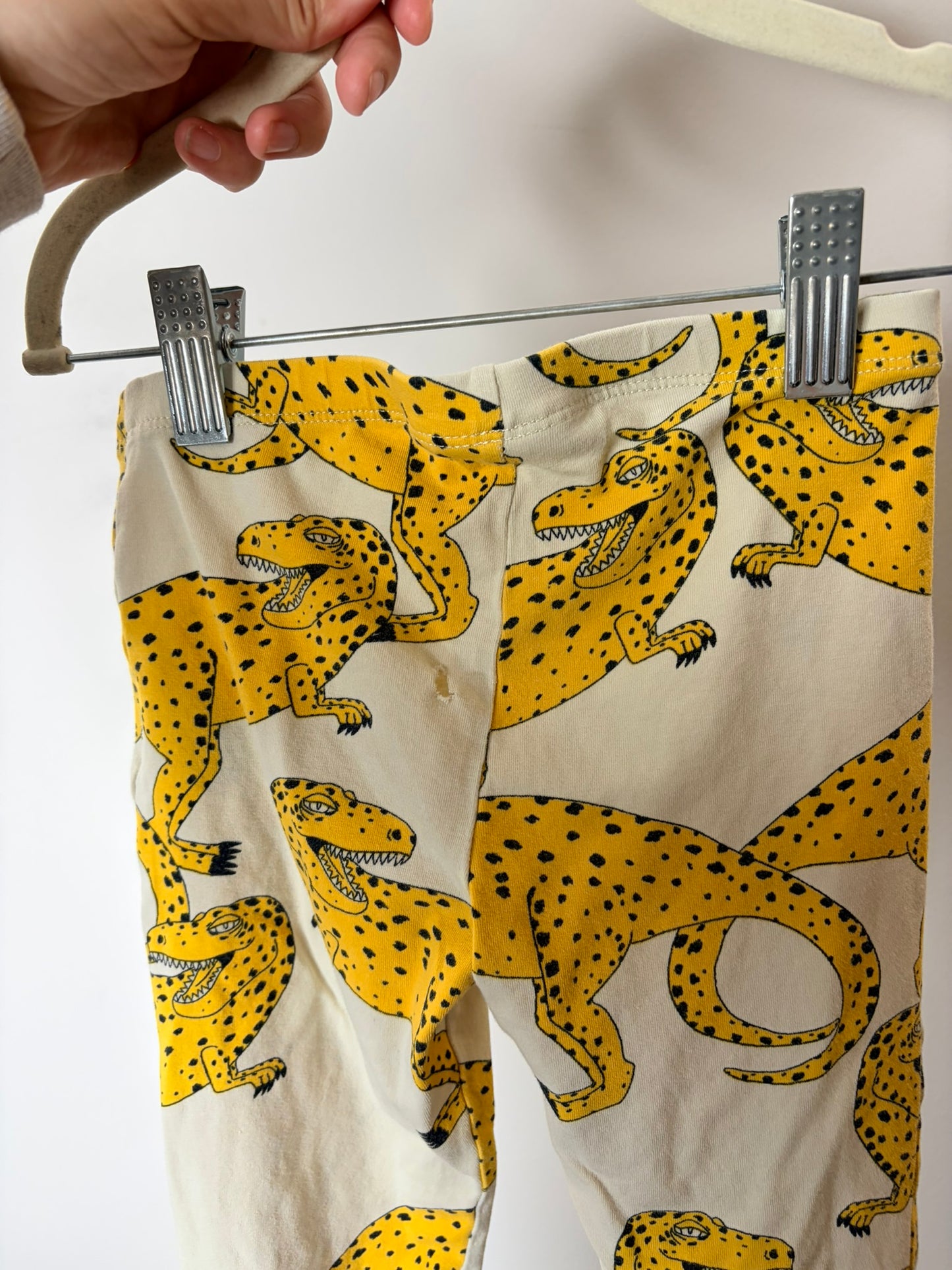 Cream leggings with a bold yellow leopard print, displayed against a white brick wall.