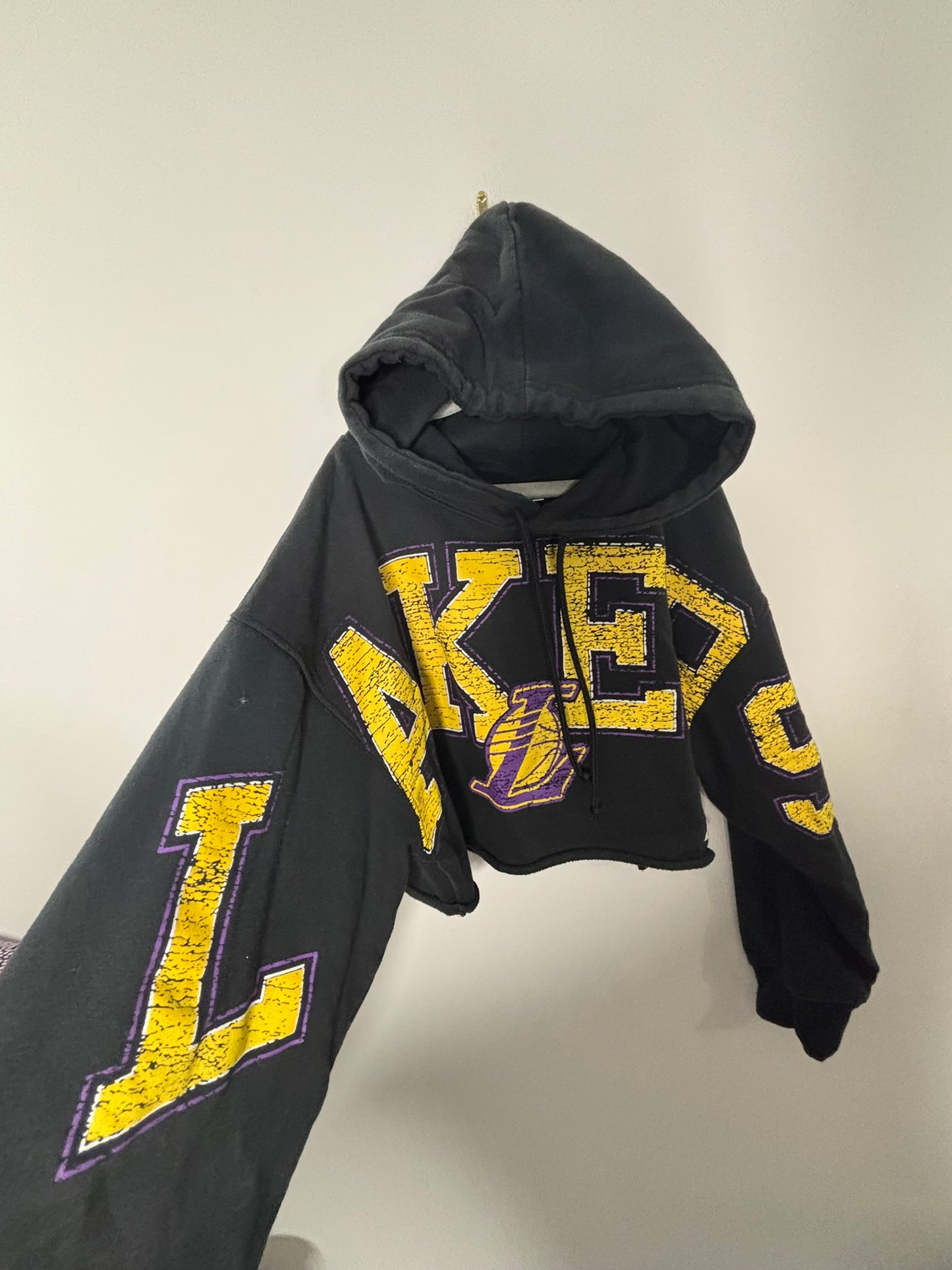 Black cropped hoodie with yellow and purple Lakers logo and text design.