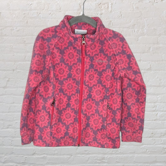 Pink and purple floral patterned fleece jacket by Columbia with a full zip and pockets, hanging against a white brick wall.