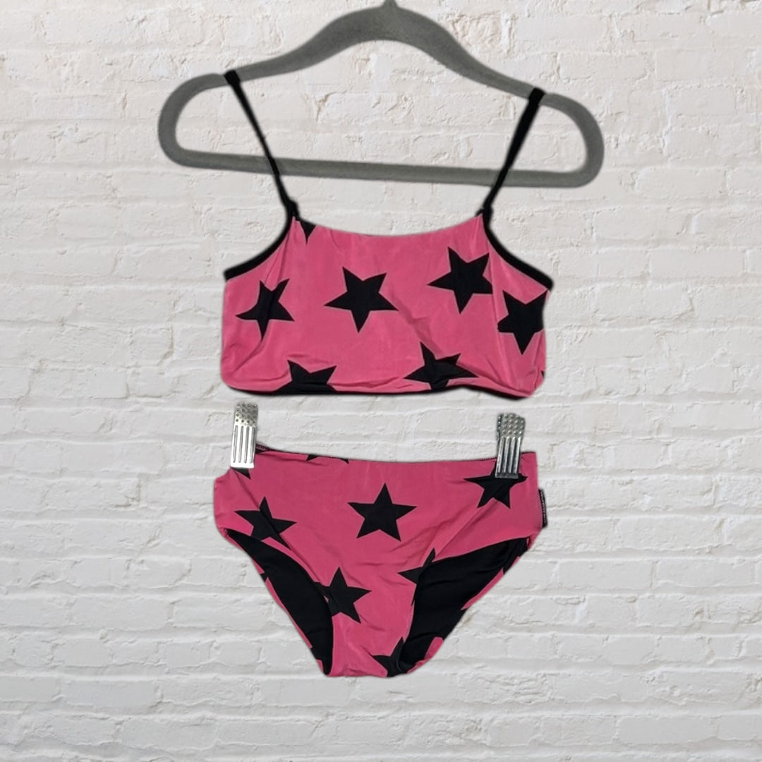 Pink bikini set with black star pattern hanging on a hanger against a white brick wall.