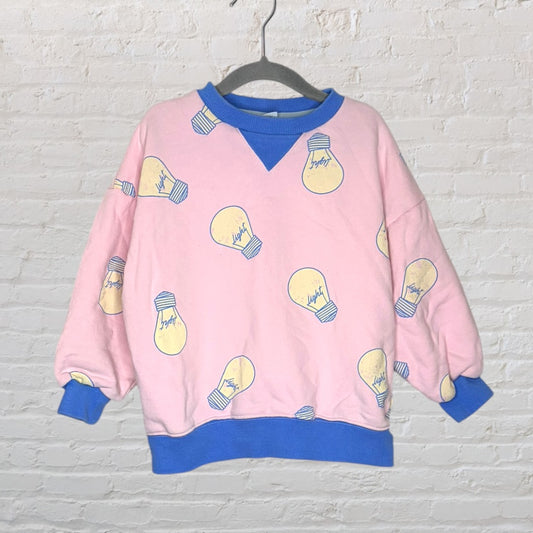 Pink sweatshirt with light bulb graphics and blue ribbed cuffs, hem, and neckline, hanging on a hanger.