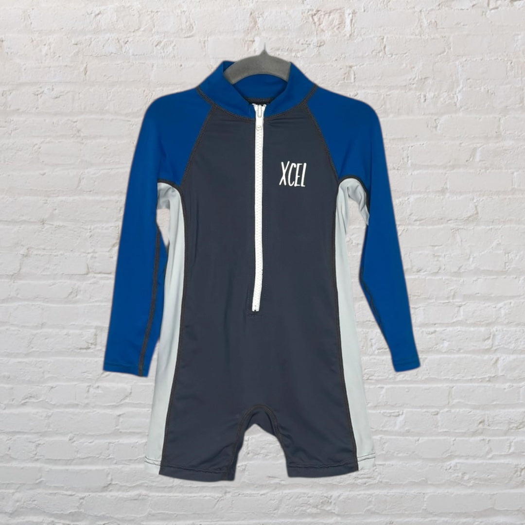 XCEL long sleeve rash guard onepiece in blue and grey with a front zip closure, displayed on a hanger against a white brick wall.